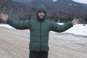 A man wears a custom Goosefeet Gear green zippered down jacket in the snow