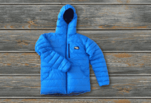 A zippered front custom Goosefeet Gear blue down jacket on lies flat on a wooden background.