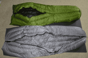 Back (bottom) view of two Goosefeet Gear custom down quilts. The top quilt is green with a partial closed back. The bottom quilt is grey with a zipperr closure.